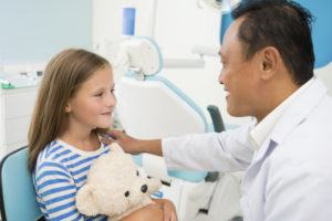 Dentist touching shoulder of his young patient to support her